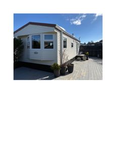 Fotografi av en hvit, panelt husvegg med et utbyggingsvindu (bryggevindu) og en terrasse foran.