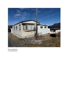 Fotografi av en hvit, enetasjes bolig sett fra siden, med en blå himmel og fjell i bakgrunnen.