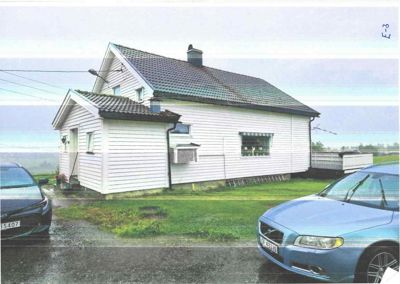 Fotografi av en hvit, trepanelert enebolig sett fra siden. Bildet viser husets fasade, tak, vinduer, en utvendig klimaanlegg, samt en del av en bil og en gate i forgrunnen.