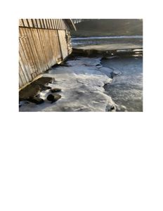 Fotografi av en bygning med trevegger og en islagt vannflate i nærheten.