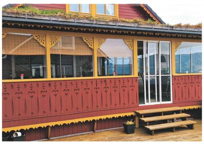 Fotografi av fasaden på en bygning med rød og gul farge, dekorative detaljer, store vinduer og en terrasse.