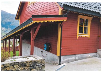 Fotografi av en rød og gul malte bygning med etasjehus, takrenner og en steinmur i forgrunnen.