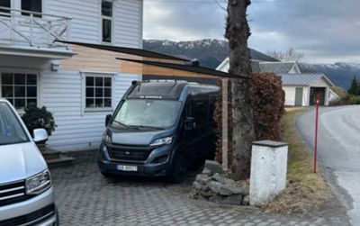 Fotografi av en eksisterende bygning med en bil parkert foran, og en tegnet skyggeprosjeksjon (en mørk trekant) lagt over bildet for å illustrere solposisjon eller skyggefall.