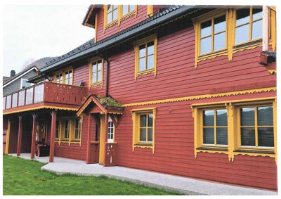 Fotografi av en rød og gul malte trebygning med etasjer, balkong og vinduer.
