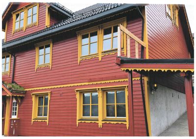 Fotografi av fasaden på et rødt trehus med gule vindusrammer og dekorative detaljer.