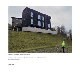 Fotografi av en mørk, moderne bygning på en skråning med en person i gul vest foran. Bildet viser en eksisterende eller ferdig bygning.