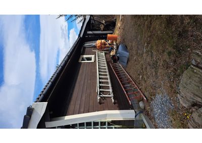 Fotografi av en mørkbrun hytte eller hus med en hvit ramme rundt et vindu. Bildet viser også en trapp, en røff, en betongblander og en hjulbar kasse på en grus- og grasmengd.