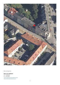 Luftfoto av et byområde med flere bygninger, jernbanespor og en markert rød prikk på en av bygningene.