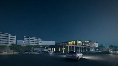 3D-visualisering av en bygning ved kveldstid med parkerte biler og lysende skilt.