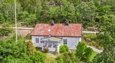 Fotografi av en hvit hytte med rødt tak, sett fra lufta eller et høyt punkt, omgitt av skog og vegetasjon.