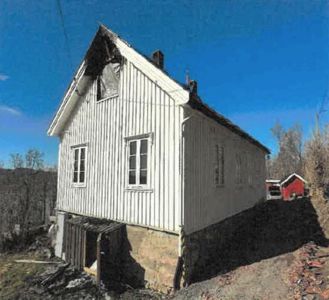 Fotografi av en hvit, trepanelert bygning med steinfundament, sett fra en vinkel som viser både front og side.