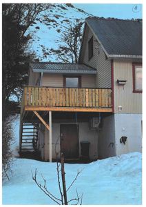 Fotografi av en bolig med en utvendig trapp opp til et balkongterrasse, sett fra bakken i snø.