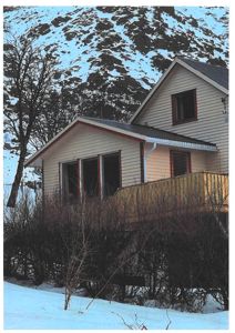 Fotografi av en hytte med snødekte bakgrunn og skog.