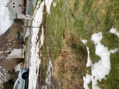 Fotografi av en tomt med snø, grøft og nabolagshus.