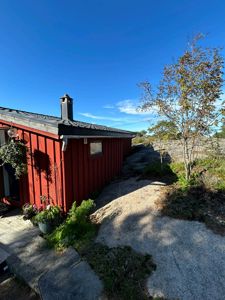 Fotografi av en rød hytte sett fra siden, med omgivelser som stein og trær.
