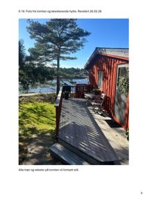 Fotografi av en eksisterende rød hytte med terrasse, sett fra siden. Bildet viser også en del av tomme, trær og vann i bakgrunnen.