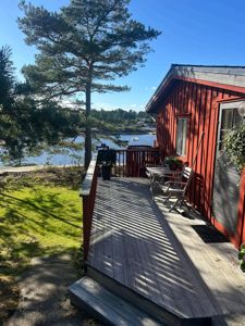 Fotografi av en rød hytte med etasjeterasse og utsikt over vannet.