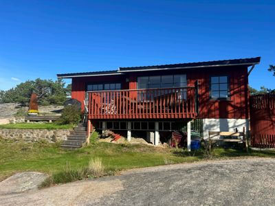 Fotografi av en rød, toetasjes hytte eller villa med en stor terrasse, sett fra en vinkel som viser både fasade og situasjon.