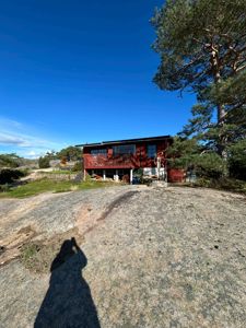 Fotografi av en rød villa med etasjehøyde, plassert på en steinete bakke under blå himmel.