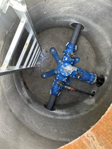 Fotografi av en blå ventilasjonsanordning (troll) installert i en betongrør eller manuell åpning.