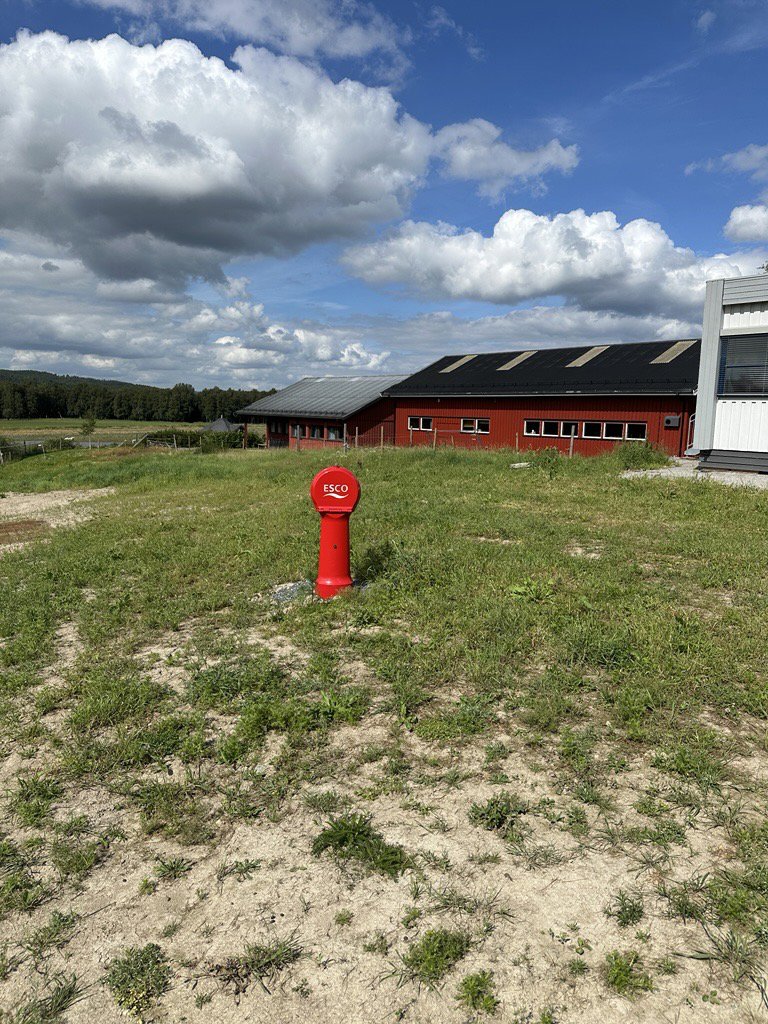Fotografi av en tomt med en rød bygning i bakgrunnen og et rødt vannhull i forgrunnen.