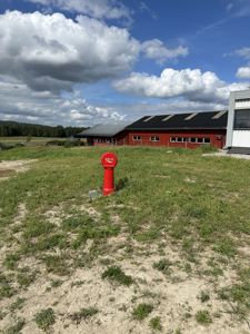 Fotografi av en tomt med en rød bygning i bakgrunnen og et rødt vannhull i forgrunnen.
