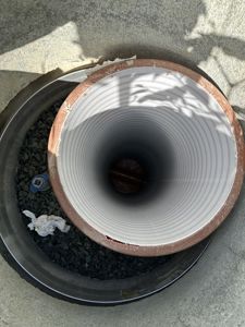 Fotografi av en nedløpsrør (tømringsrør) sett ned i en utløpsbrønn eller grøft.