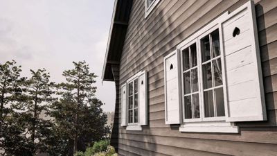 Fotografi av fasaden på en hytte eller hus med trepanel, hvite vinduer og skuffer.