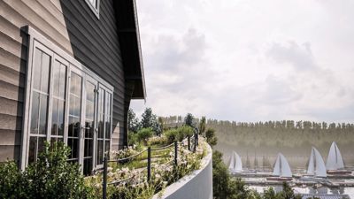 3D-visualisering av en husfasade med utsikt over en havn med seilbåter.