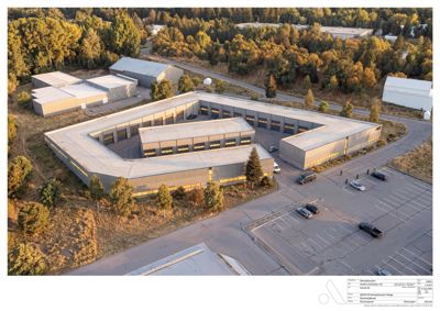 Luftfoto av en industriell bygning med parkeringsplass og omgivende natur.