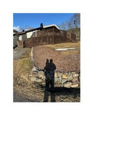 Fotografi av en eksisterende eller ferdig bygning sett fra bakkenivå, med fokus på fasade, terrasse og steinmur.