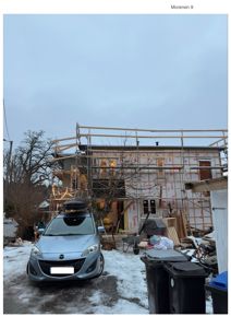 Fotografi av en bygning under oppføring (scaffolding, isolasjon, takkonstruksjon) med bil og utstyr foran.