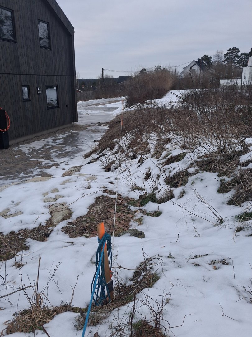 Fotografi av en bygning med mørk fasade, snø på bakken og en markørstang i forgrunnen.