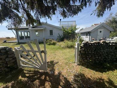 Fotografi av en hvit, enetasjes bygning med en steinmur og en hvit gate i forgrunnen.