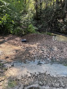 Fotografi av et utgravet område i skog med en pipe og en grøft.