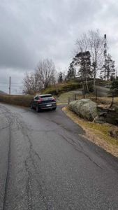 Fotografi av en bil som kjører på en vei i et naturområde med trær og steiner.
