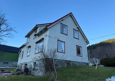 Fotografi av en hvit, to- eller treetasjers bygning med hvitlistet fasade og steinfundament, sett fra siden.