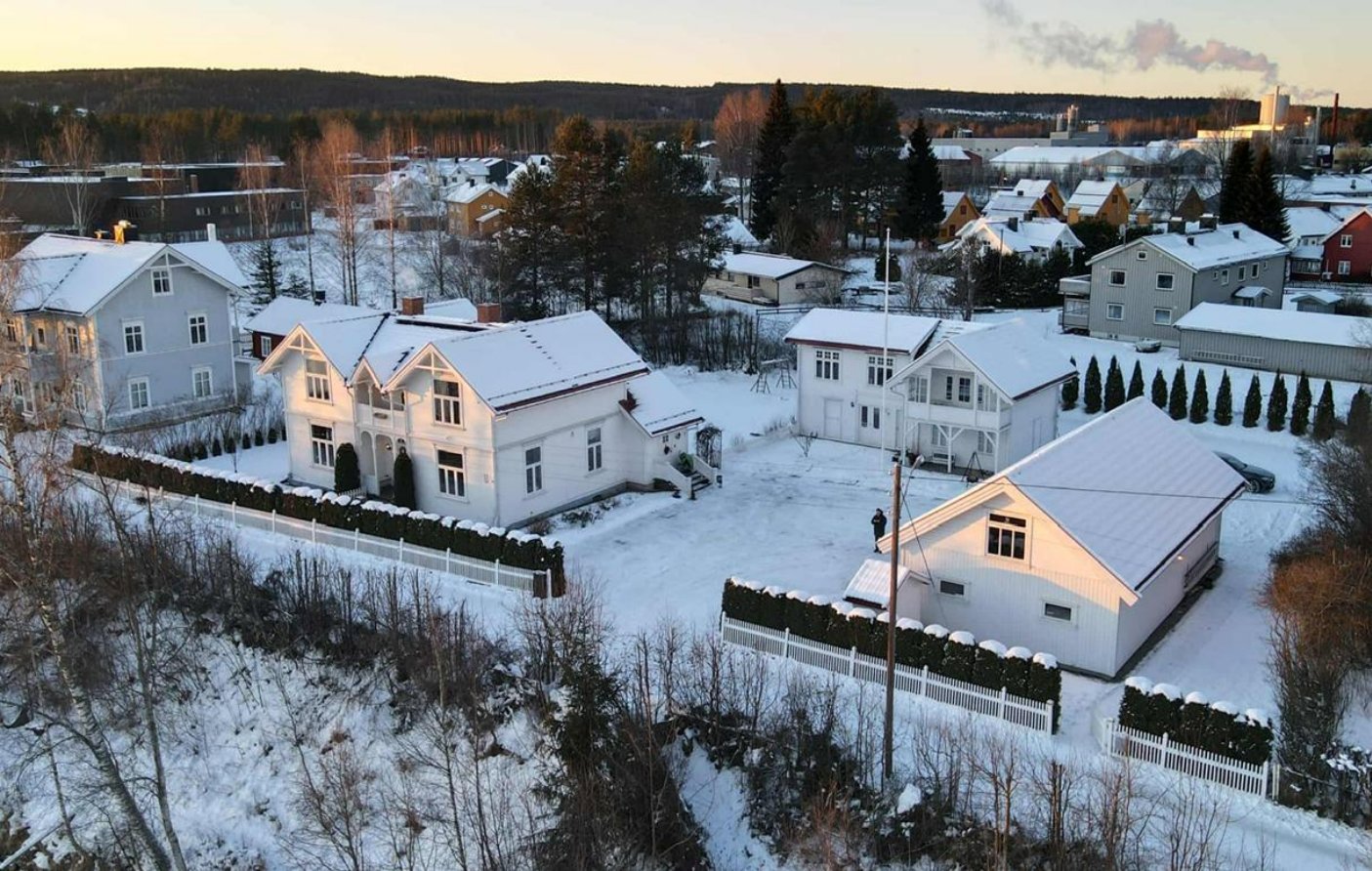 Fotografi av en boligbebyggelse i vinterlandskap med snødekte hus og trær.