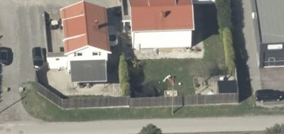 Luftfoto (aerial view) av en tomt med to hus, en hekk og parkerte biler.