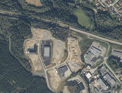 Flyfoto eller satellittbilde som viser et industriområde med flere bygninger, veier og omgivende natur.