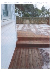 Fotografi av en uteplass (terrasse) med trapp opp til en bygning, med snø på gulvet og bakgrunn av skråning.