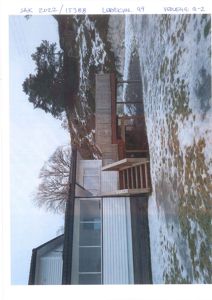 Fotografi av en eksisterende eller planlagt bygning med en terrasse og trapp, sett fra bakkenivå. Bildet viser også omgivelser med snø og skog.