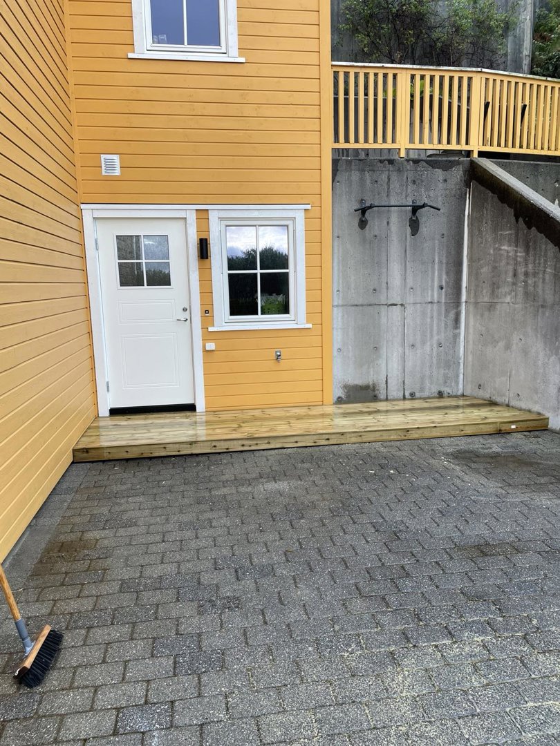 Fotografi av en ferdig eller nesten ferdig bygning med gul fasade, hvit dør, vinduer, en ny anlagt trapp og en betongvegg.