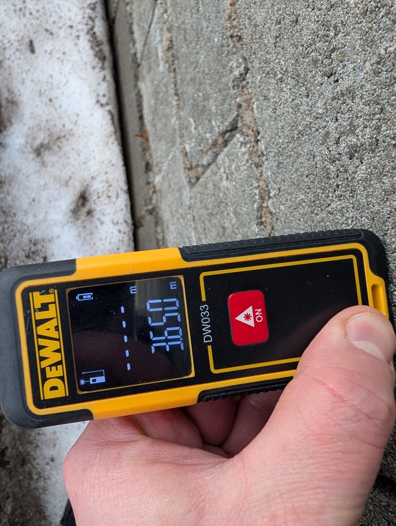 Fotografi av en person som holder en laseravstandsmåler (DeWalt DW033) opp mot en betongvegg. Måleren viser en avstand på 3,650 meter.