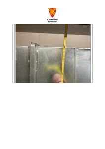 Fotografi av en metallvegg eller panel med en gul målebånd som er plassert vertikalt langs overgangen mellom veggen og taket.