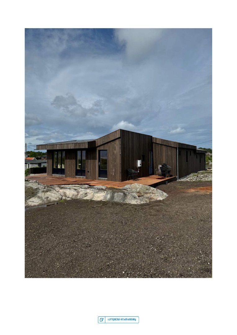 Fotografi av en ferdigbygd eller ferdigstilt moderne hytte med mørk fasade og terrasse.