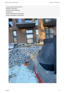 Fotografi av en byggeplass med en nybygd leilighetsblokk i bakgrunnen. I forgrunnen er det en grøft fylt med stein og grus, samt en stor svart tank (sannsynligvis for avløpsvann eller regnvann) som er dekket med plast. En oransje gaffeltruck er synlig midt i bildet.