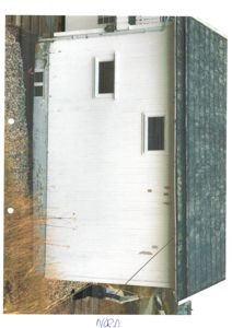Fotografi av en hvitmalt fasade på en bygning sett fra siden, med skriftlig notat 'NORD' som indikerer retning.