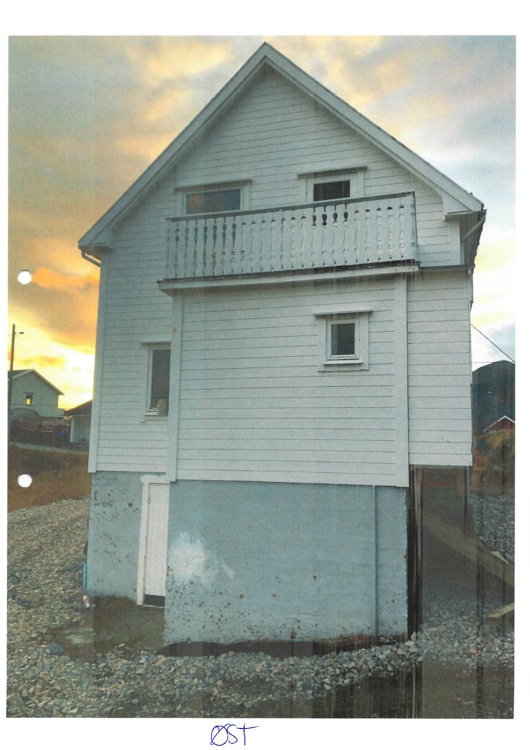 Fotografi av en hvit, to- eller treetasjes bygning med et balkong på øverste etasje, sett fra øst mot en solnedgang.