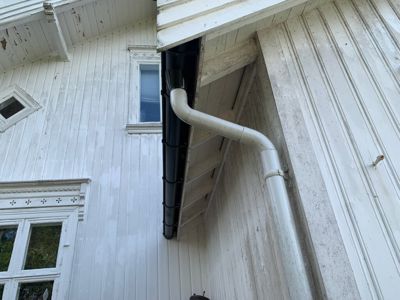 Fotografi av en hvit malte trefasade med et svart nedløp og en hvit nedløpsrør som går nedover.